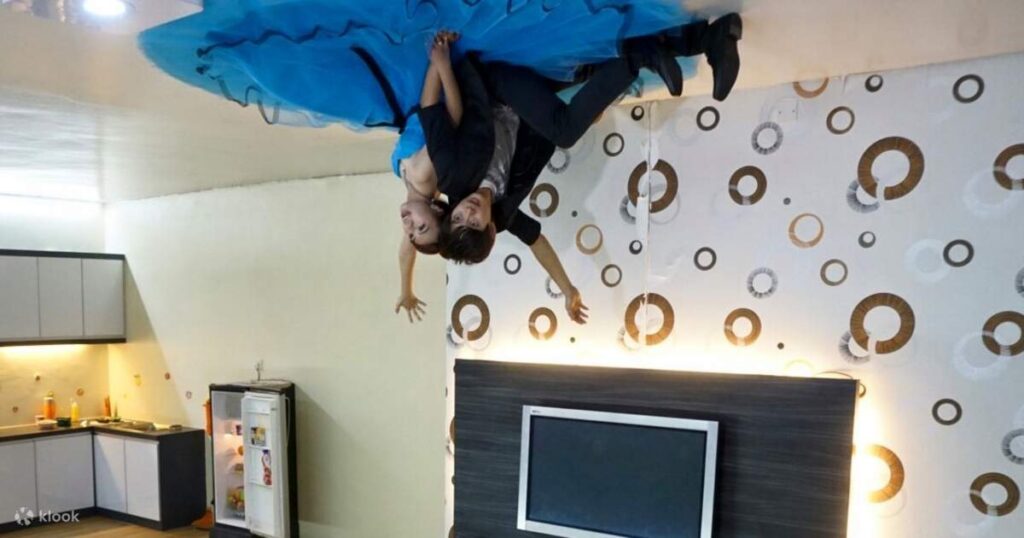 A couple posing as if standing on the ceiling inside the inverted room of the Upside Down House