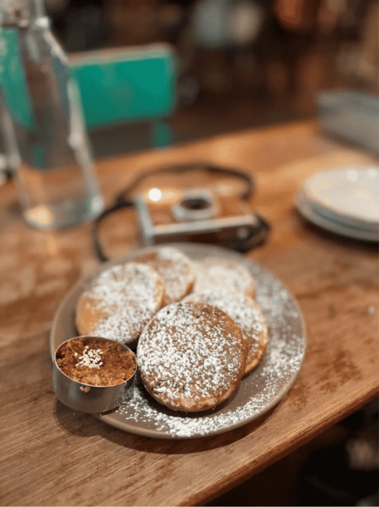 A plate of sugar-dusted gula melaka pancakes on a wooden cafe table