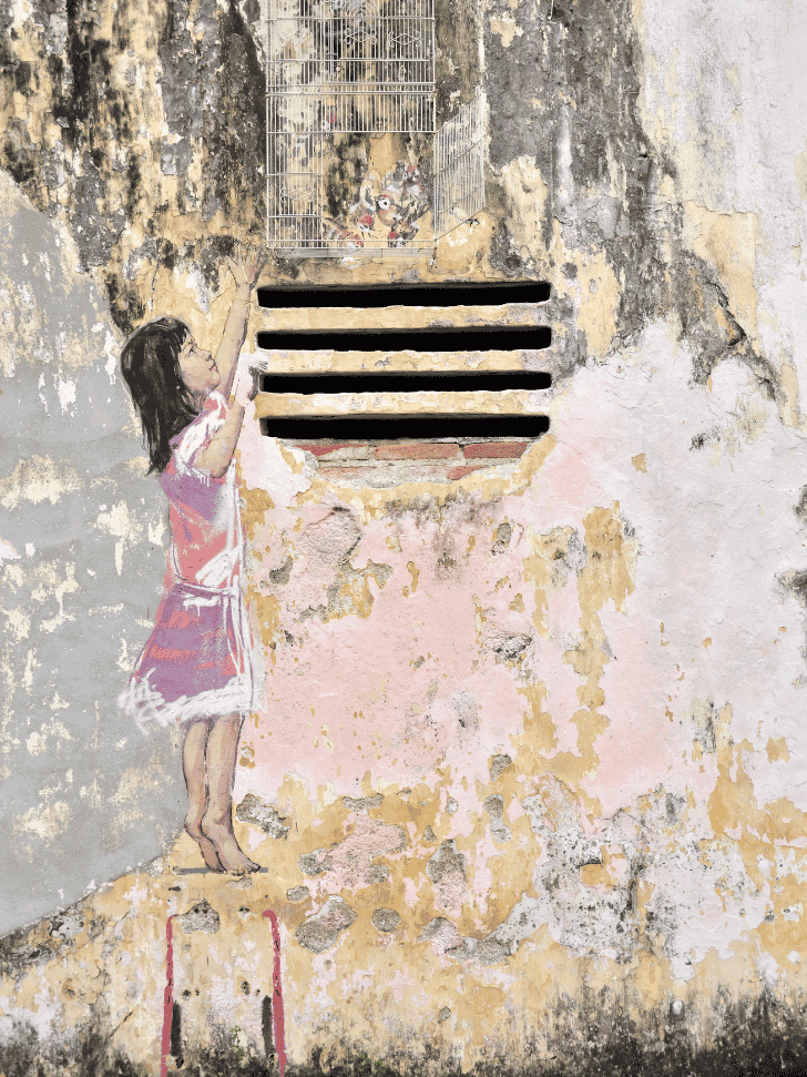 Street mural of a young girl reaching up toward a birdcage on a weathered Ipoh wall