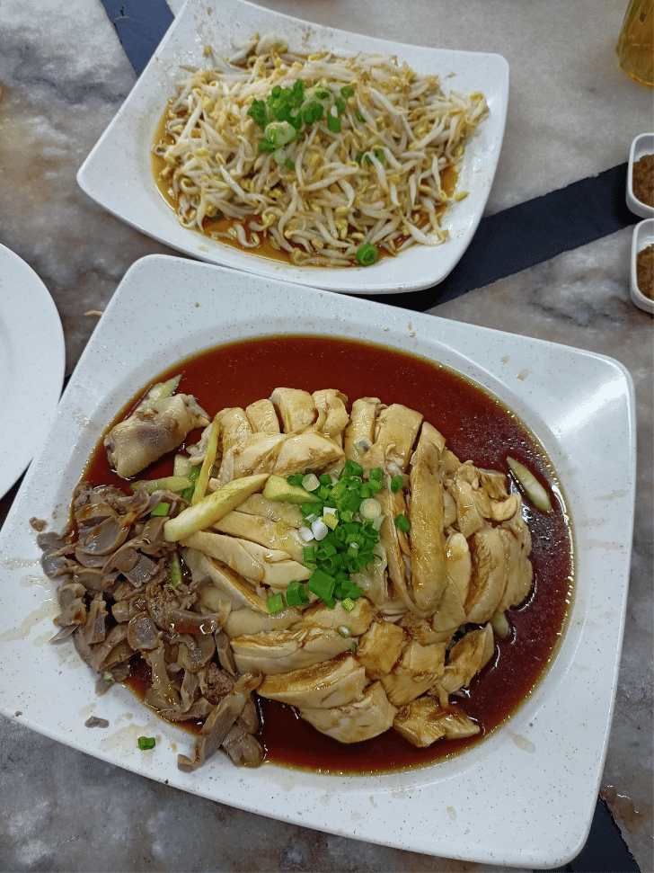 A plate of poached chicken in soy sauce beside a plate of stir-fried bean sprouts