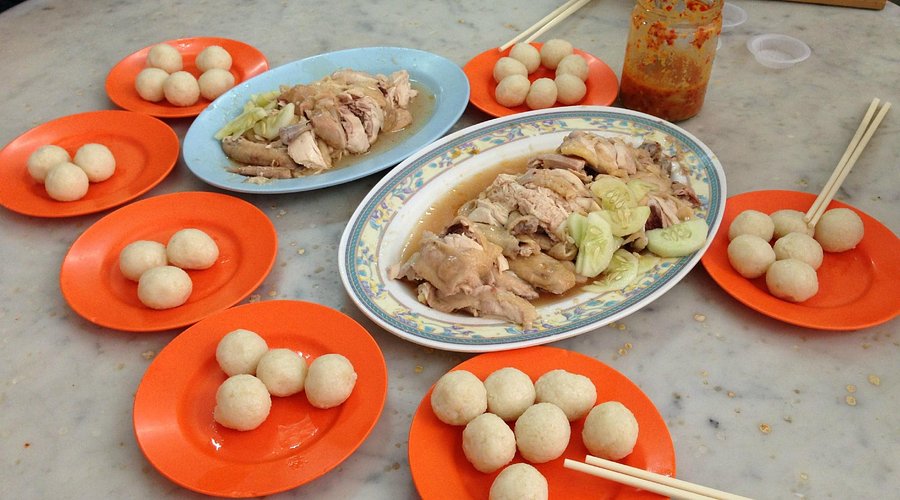 Plates of sliced chicken and orange dishes of rolled chicken rice balls on a marble table