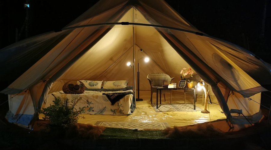 A lit safari-style bell tent with a bed and seating inside at night near Gopeng