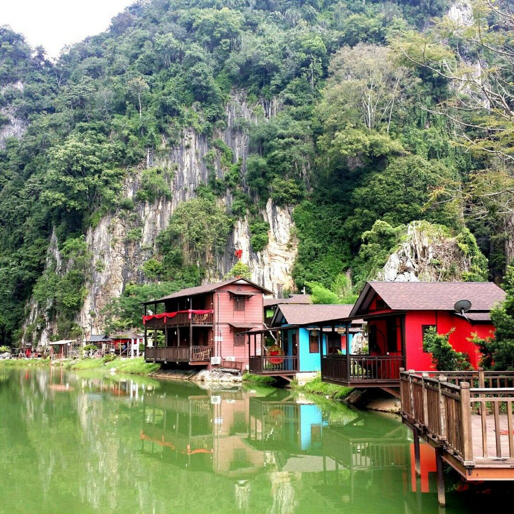 Colourful wooden chalets on stilts reflected in a green lake below limestone cliffs at Qing Xin Ling