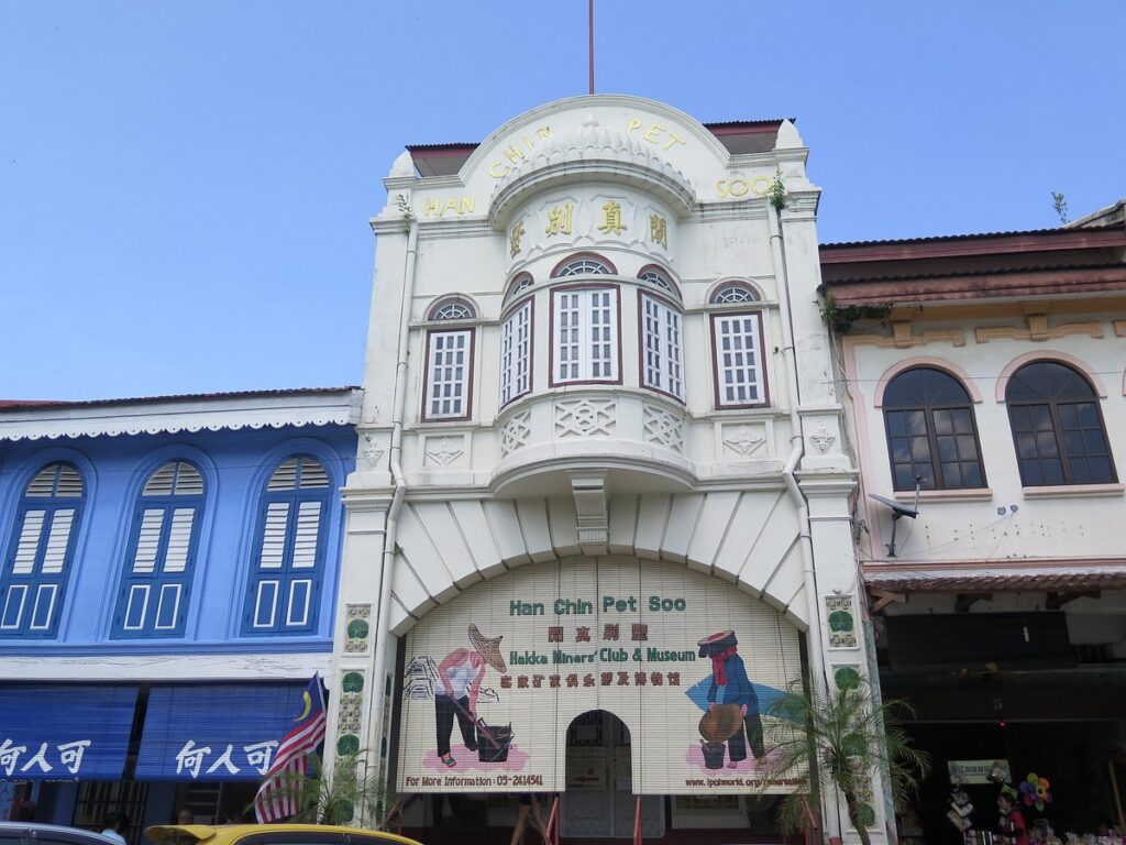 The white heritage facade of Han Chin Pet Soo, Ipoh's Hakka tin-mining museum, beside a blue shophouse