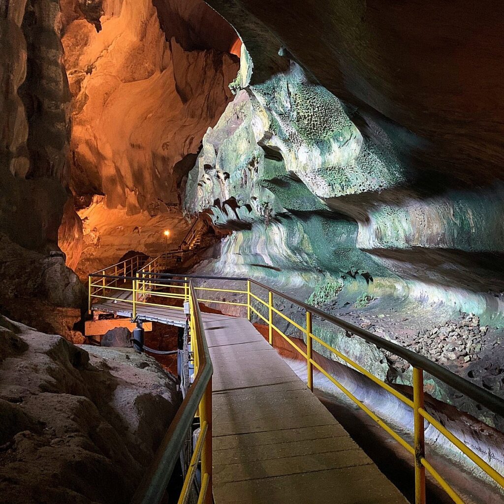 A lit boardwalk with yellow railings winding through the illuminated chambers of Gua Tempurung cave