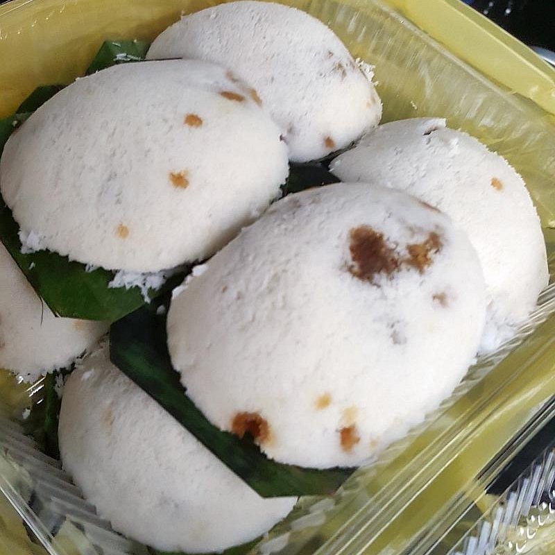 Steamed white putu piring rice cakes with molten gula melaka centres in a takeaway box