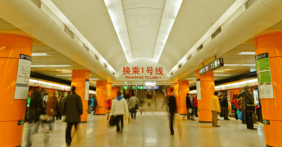 Passengers walking through a Beijing subway concourse with orange pillars and Line 1 signage