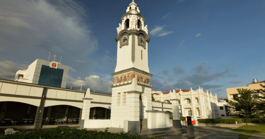 The white Birch Memorial Clock Tower with painted panels against a blue sky in Ipoh