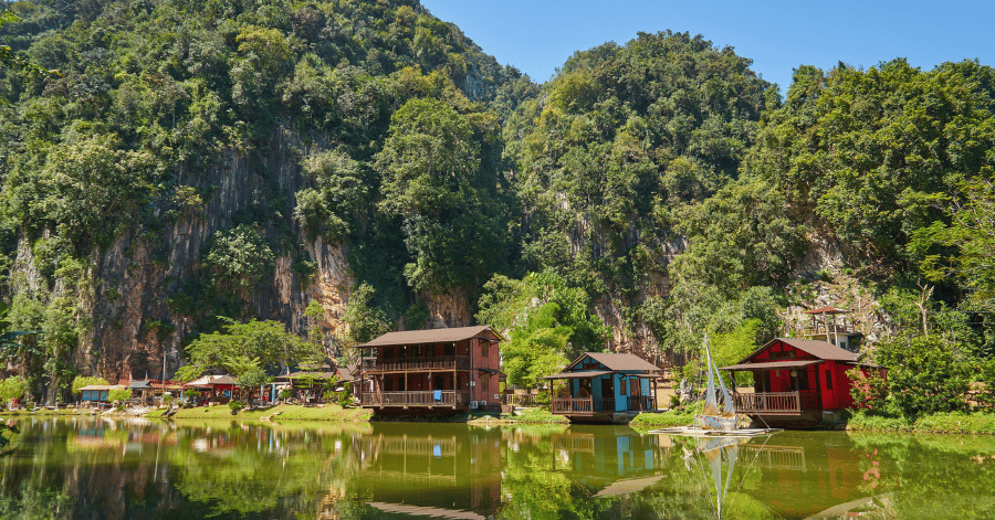 Colourful wooden chalets on a still lake beneath jungle-covered limestone cliffs near Ipoh