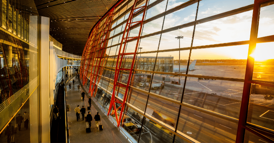 Sunlight streaming through the red-framed glass facade of a modern Beijing airport terminal