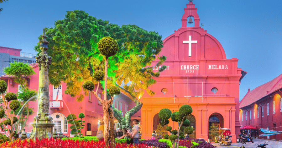 The red Christ Church and bell tower at Malacca's Dutch Square, framed by garden topiary