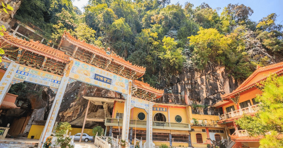 An ornate orange-roofed Chinese temple built against a jungle-covered limestone cliff in Ipoh
