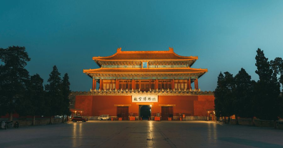Illuminated red-and-gold traditional Beijing pavilion glowing against a deep blue dusk sky