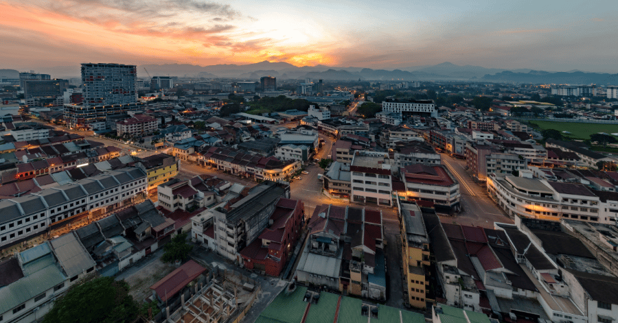 Aerial view of Ipoh's rooftops at sunset with mountains along the orange horizon