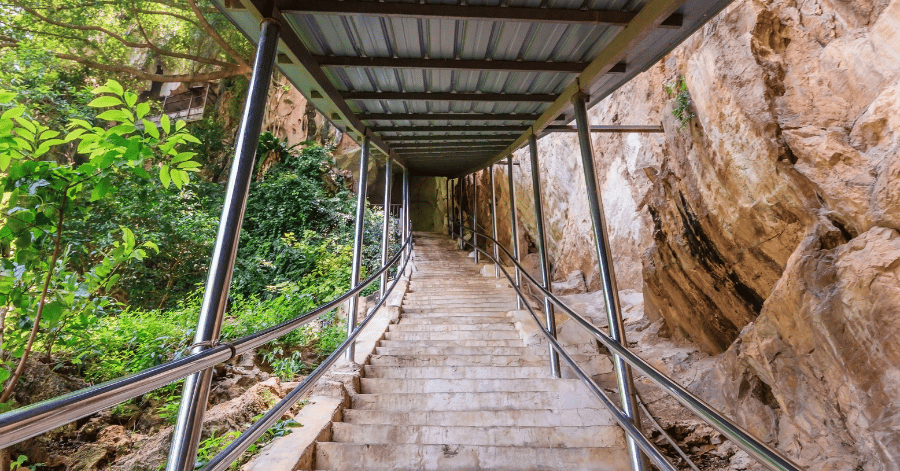 A covered concrete staircase with metal railings climbing beside a limestone rock face