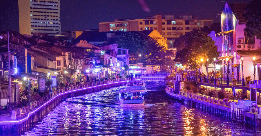 The Malacca River glowing with purple and neon lights reflected on the water at night