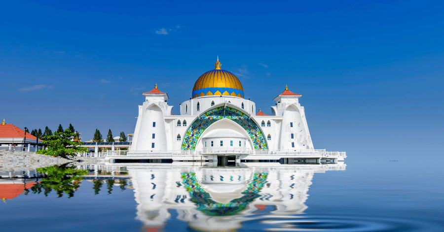The white-and-gold Malacca Straits Mosque reflected in calm water at high tide