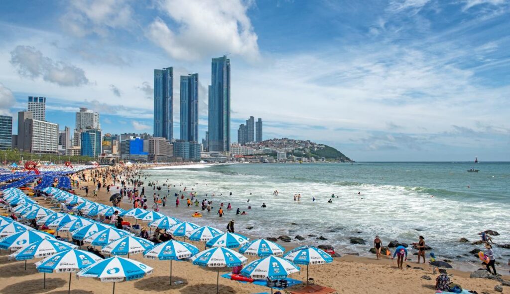Crowds and blue parasols on Haeundae Beach with high-rise towers behind