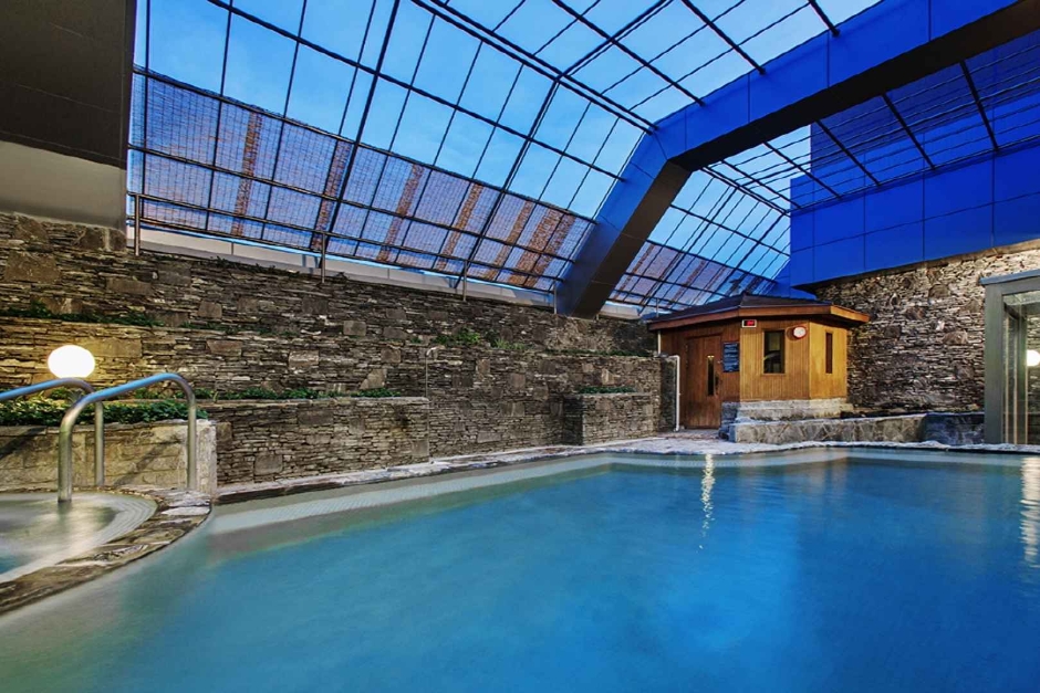 Indoor hot-spring pool under a glass roof with a wooden sauna hut