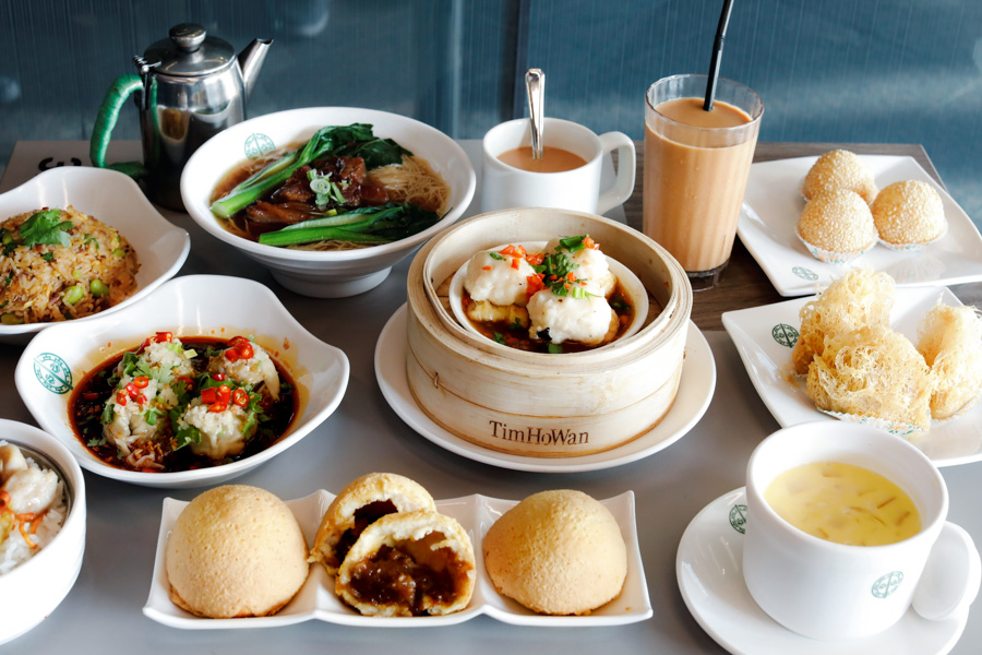 A table of Tim Ho Wan dim sum including siu mai, baked BBQ pork buns, noodles and milk tea