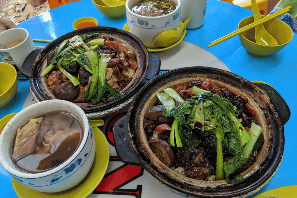 Clay pots of rice topped with Chinese sausage and greens on an outdoor table in Hong Kong