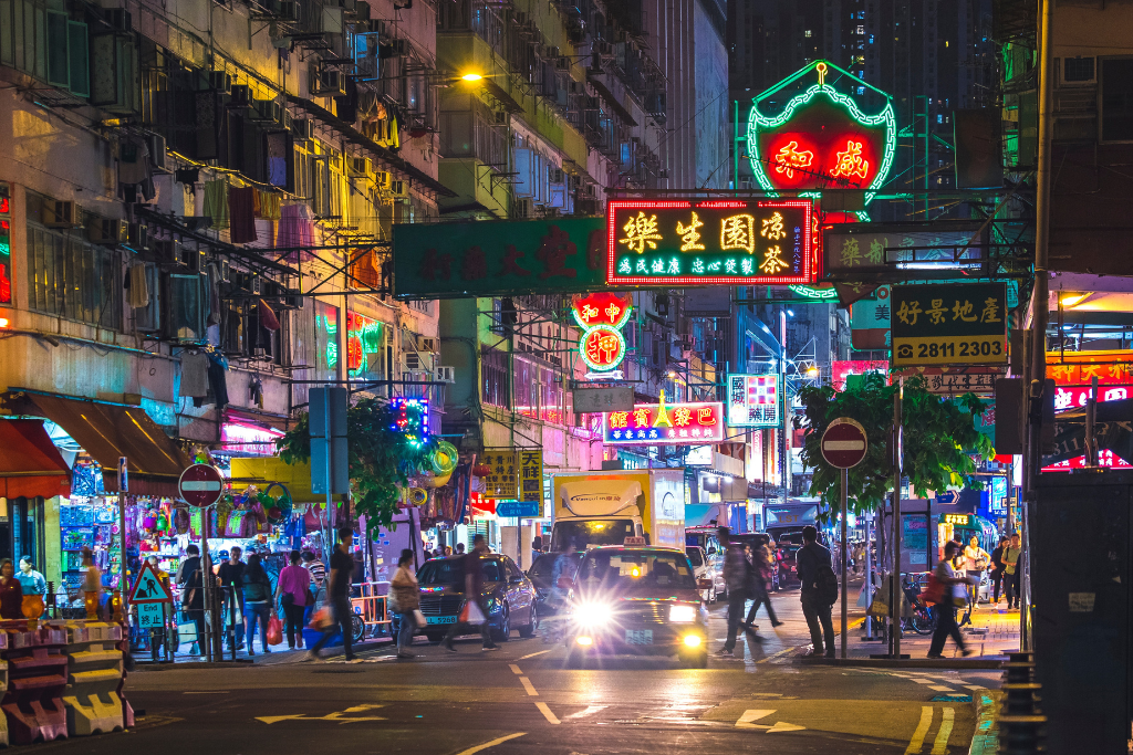 Crowds and glowing neon signs along a Hong Kong night market street after dark