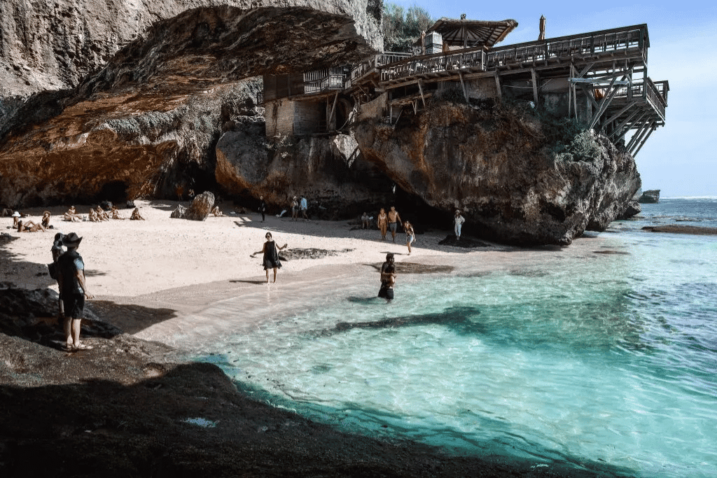 Visitors on a cave-mouth cove beach below the cliffs at Uluwatu, Bali