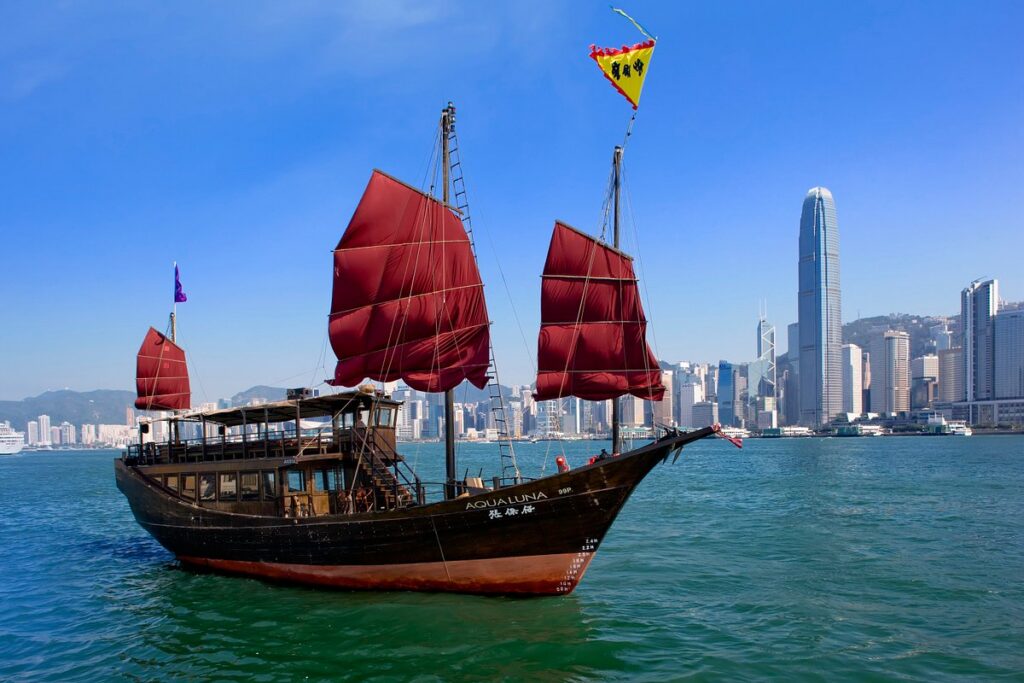 The red-sailed Aqua Luna junk boat sailing Victoria Harbour with the Hong Kong Island skyline behind
