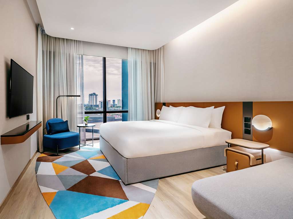 Novotel Johor Bahru room with a bright bed, blue armchair and a floor-to-ceiling city view
