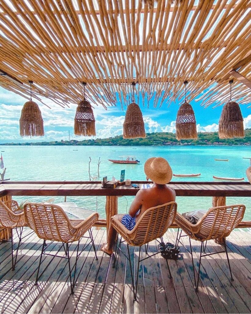 Person at a thatched beachfront bar overlooking turquoise water and boats, Nusa Ceningan