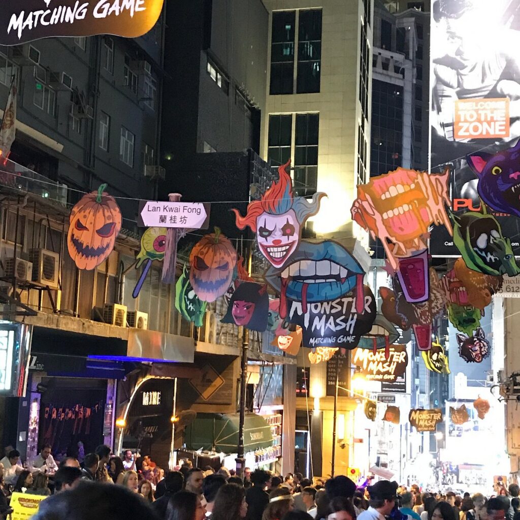 Crowds filling Lan Kwai Fong at night beneath colourful Halloween street decorations