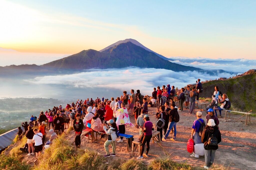 Trekkers watching sunrise over a volcano above a sea of cloud on Mount Batur