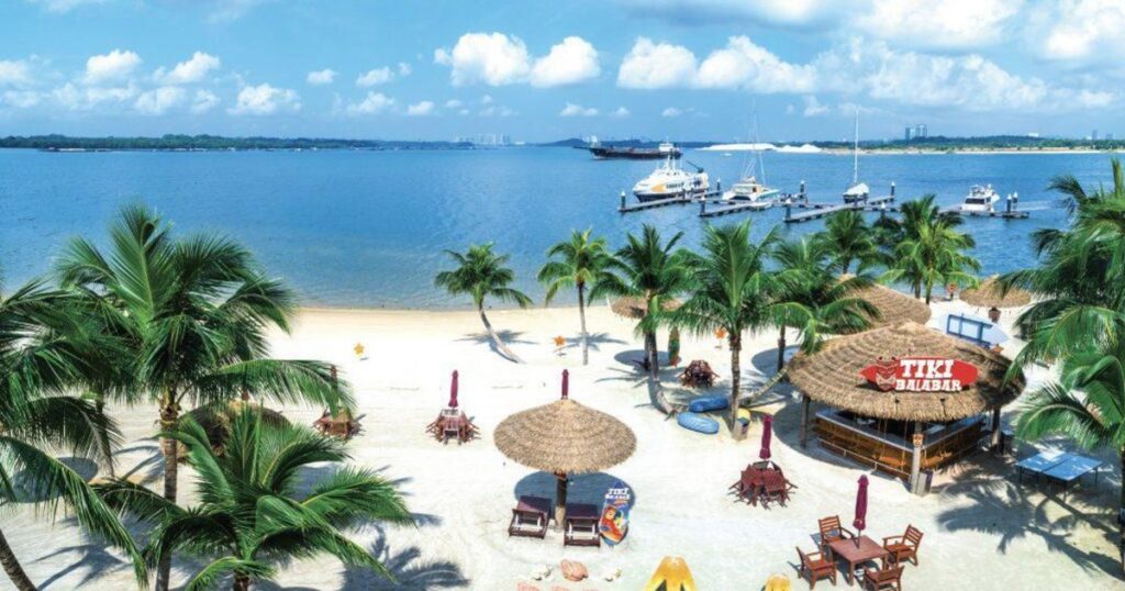 Palm-lined white-sand beach with a thatched tiki bar and a boat jetty at Danga Bay