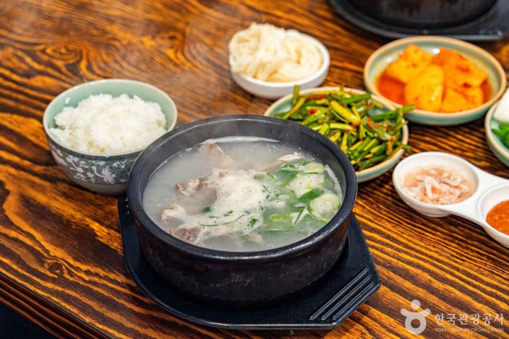 Bowl of milky dwaeji gukbap pork soup with rice and side dishes