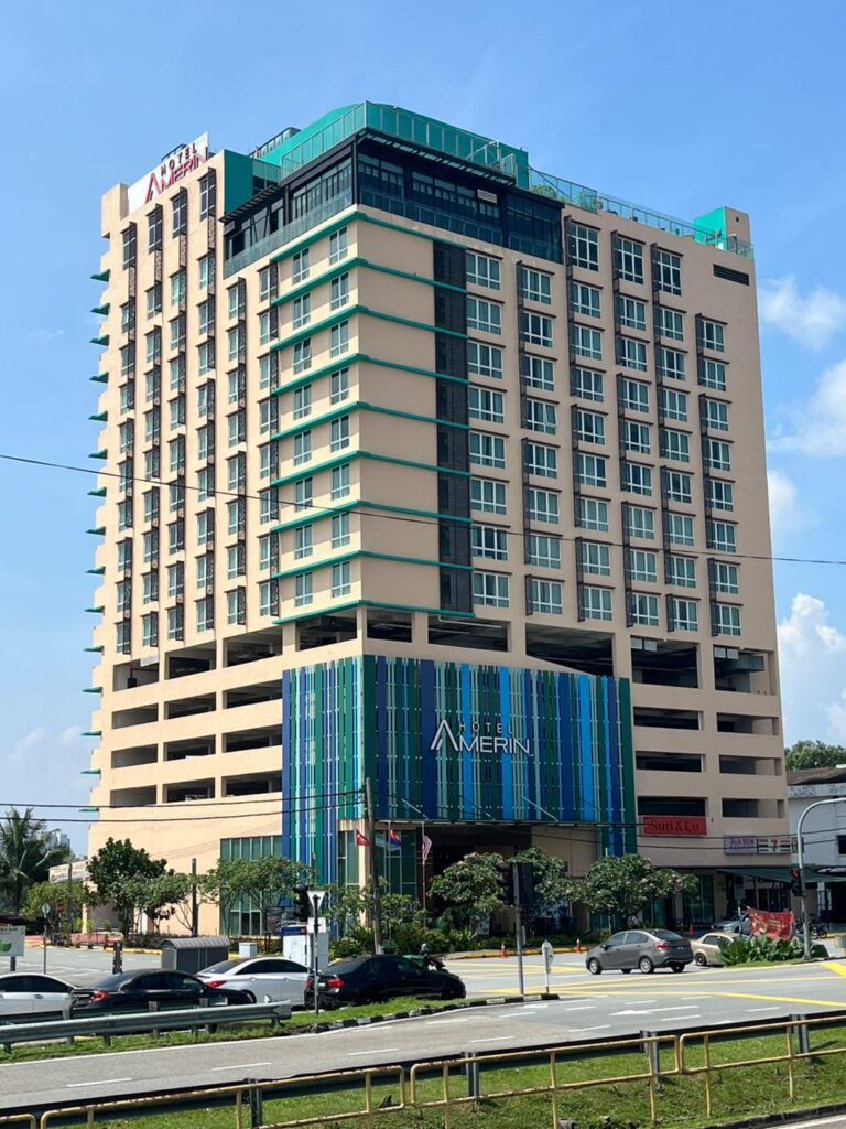 Hotel Amerin's tower with a colourful facade and signage above a Taman Perling street
