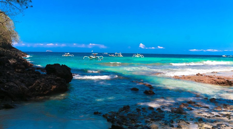 Jukung outrigger boats on clear turquoise water off a rocky Bali shore