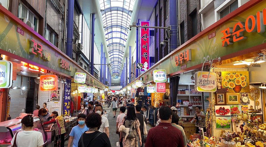 Shoppers in the covered arcade of Gukje Market lined with stalls and signs