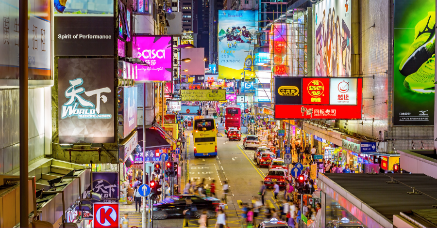 A Hong Kong shopping street glowing with towering neon billboards above busy night-time crowds and trams