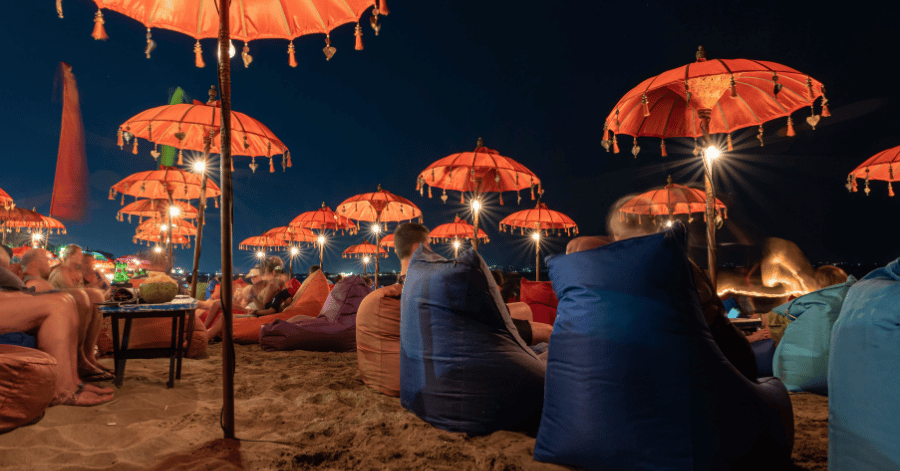 Lantern-lit Balinese umbrellas and beanbags on a Seminyak beach at dusk