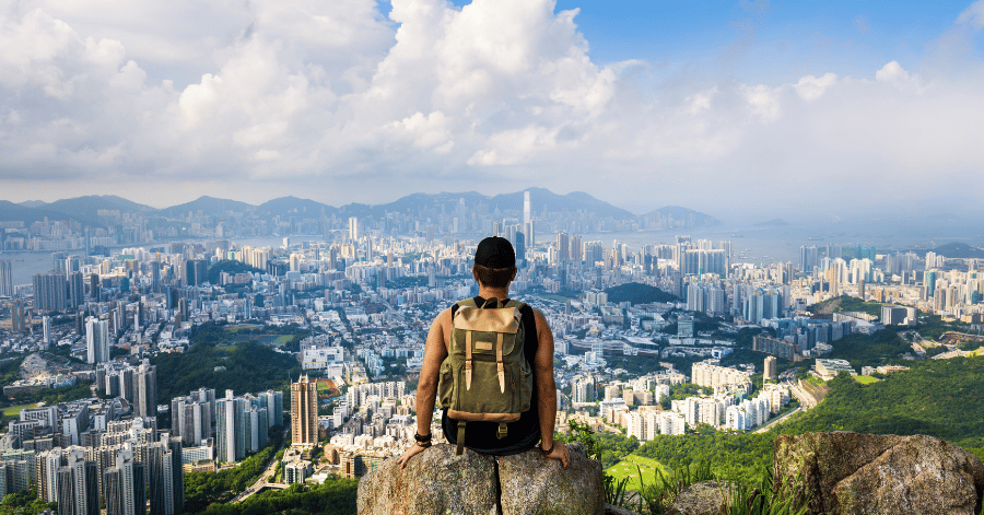 A hiker with a backpack looking out over Hong Kong's skyline and harbour from a hilltop trail