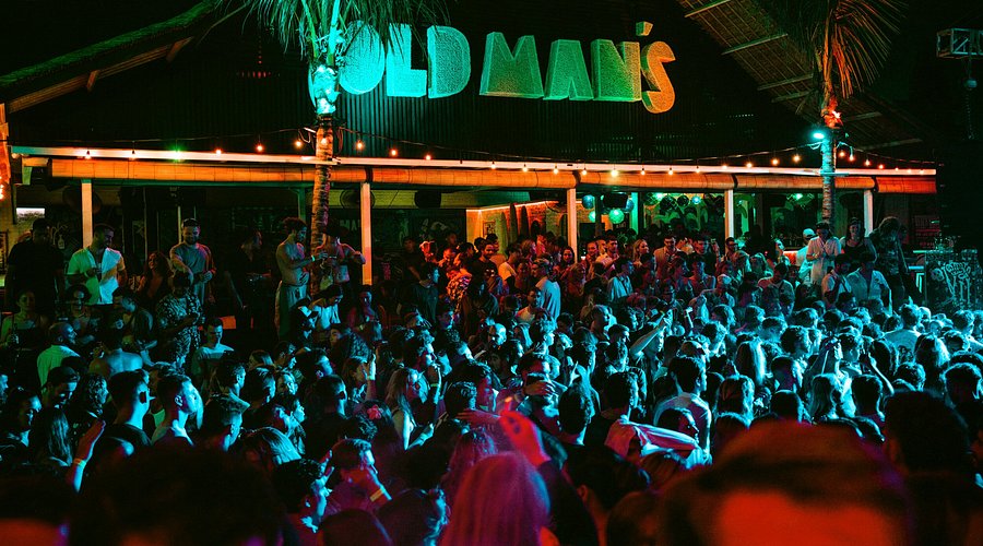 Night-time crowd in front of the neon Old Man's sign at the Canggu beach bar