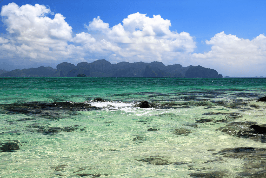 Clear turquoise water over rocks with limestone islands on the horizon, Krabi