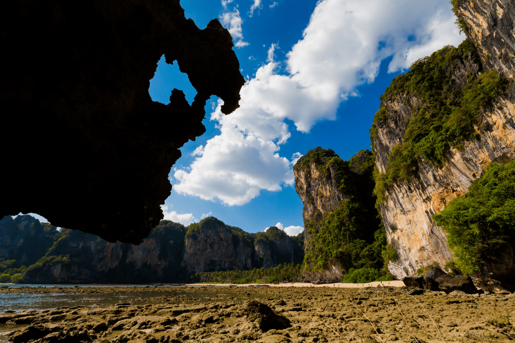 Limestone overhang framing cliffs and a rocky low-tide beach at Tonsai, Krabi