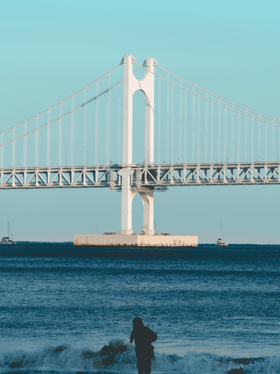 Busan's Gwangan Bridge over the sea at dusk with a surfer in the foreground