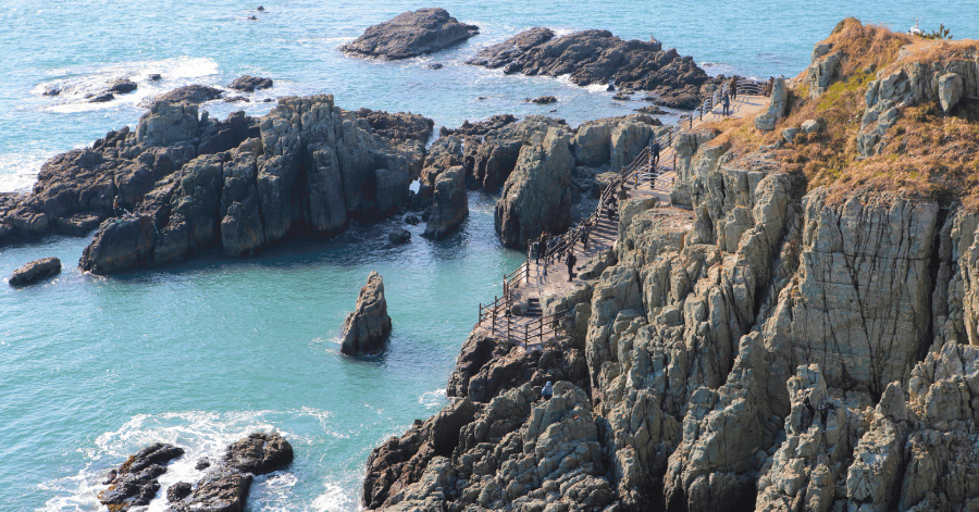 People exploring a rugged rocky coastline above turquoise sea in Busan