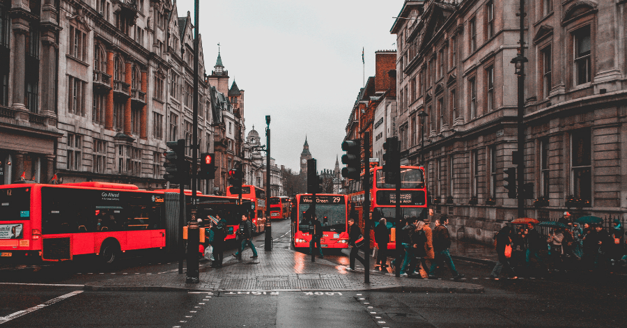 Red double-decker buses on a wet London street with Big Ben in the distance