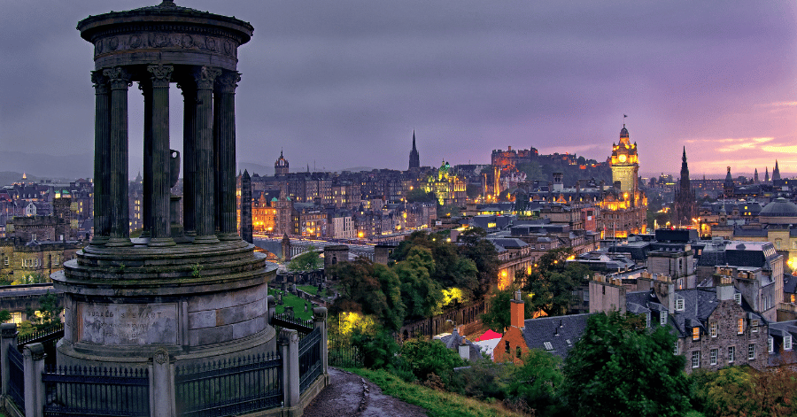 Edinburgh skyline at dusk seen from Calton Hill, with the castle and city lights in the distance