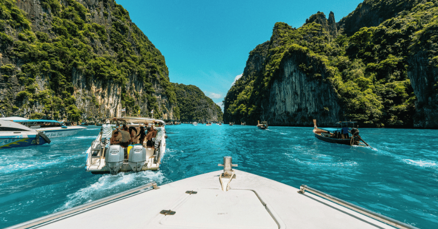 View from a speedboat cruising between green limestone cliffs on turquoise water, Krabi