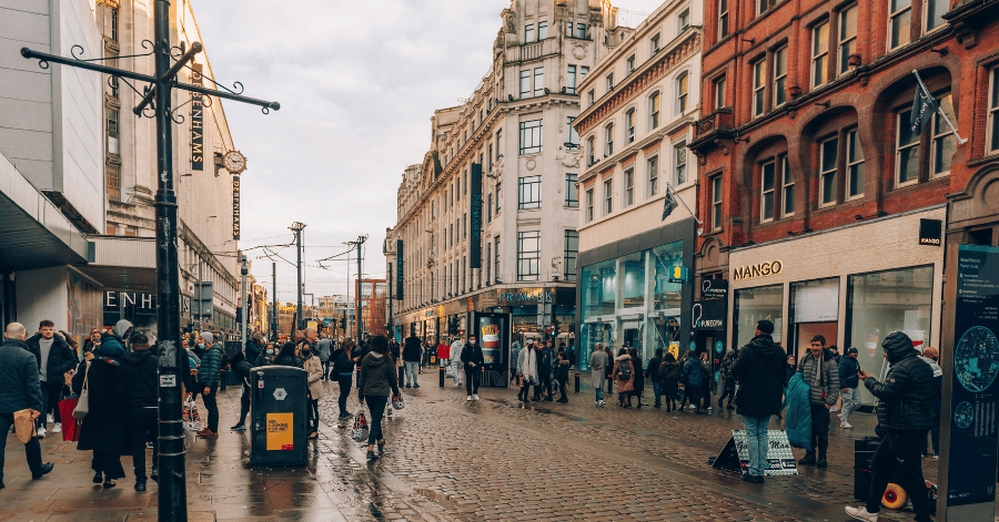 Shoppers on a busy British high street lined with shops on an overcast day
