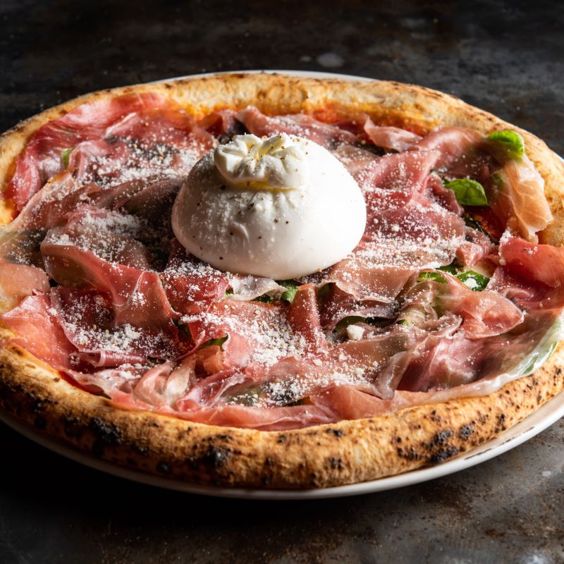 A wood-fired pizza topped with burrata cheese and Parma ham at Pizza 4P's